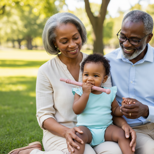 Bébé fille noire utilisant une brosse de dentition en silicone rose avec ses grands-parents au parc - Jouet de dentition sûr et non toxique pour soulager les gencives
